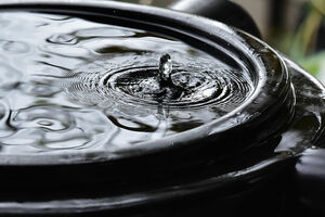 Rainwater harvesting. A collection tank full of rain water, overhead view. A drop rises up in the middle of ripples.