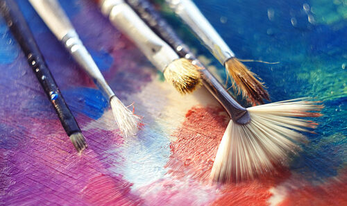 Several brushes of different shapes and with different bristles lie on the palette, illuminated by the bright sun