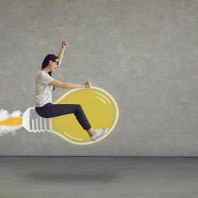 Happy modern business woman with the drive to succeed riding idea light bulb rocket