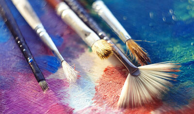 Several brushes of different shapes and with different bristles lie on the palette, illuminated by the bright sun