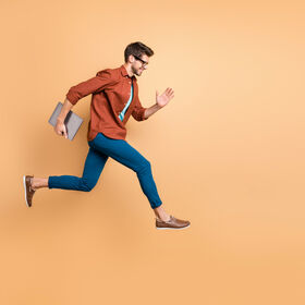 Full length body size view of his he nice attractive cheerful cheery successful brunet guy jumping in air carrying laptop running fast late hurry-up isolated over beige color pastel background