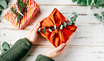 Furoshiki tissue wrapping of presents. Female hand holding a gift in eco friendly reusable fabric package. Small business, ethical shopping idea. Presents packed in plastic free. Zero waste lifestyle