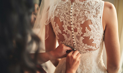 Bridesmaid helping bride fasten corset close-up and getting her dress, preparation concept in morning for wedding day.