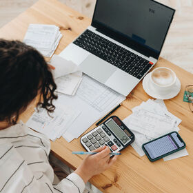 Top view of a woman working at home in the kitchen with financial papers, counting on a calculator, paying bills, planning a budget to save some money. Independent accounting, remote accountant