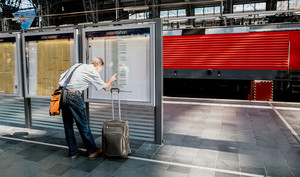 Pendler - Person auf der Reise am Gleis am Bahnhof unf schaut nach Informationen, weil der Zug Verspätung hat